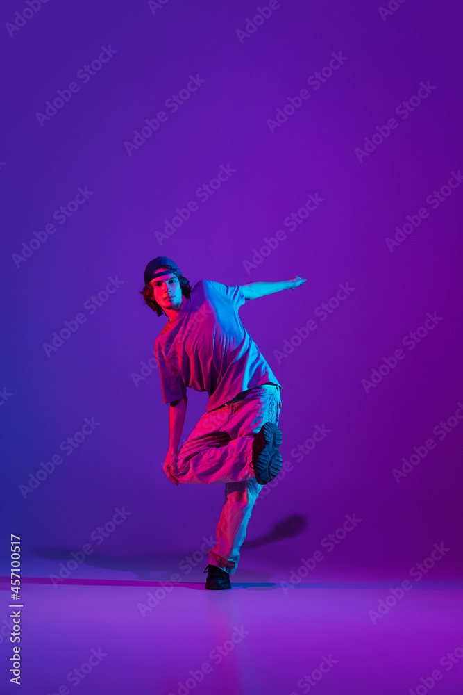 Stylish sportive boy dancing hip-hop in stylish clothes on colorful background at dance hall in neon light. Youth culture, movement, style and fashion, action.