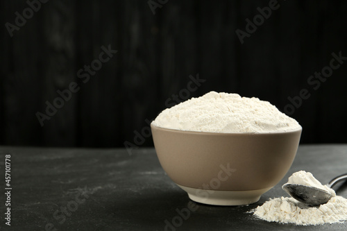 Ceramic bowl with flour on dark grey table, space for text. Cooking utensils