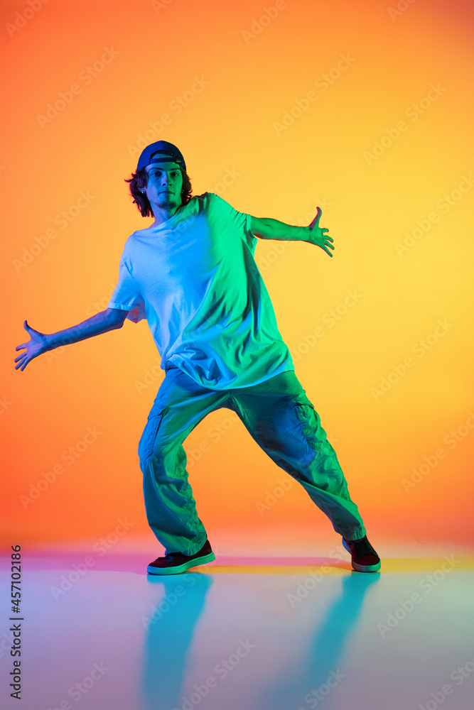 Close-up portrait of young man, hip-hop dancer in stylish clothes in action isolated on colorful background at dance hall in neon light.