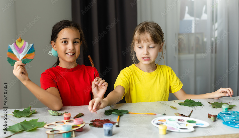 two girls paint autumn leaves at table. two girls paint autumn leaves at table.