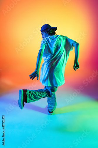 Close-up portrait of young man, hip-hop dancer in stylish clothes in action isolated on colorful background at dance hall in neon light. © master1305