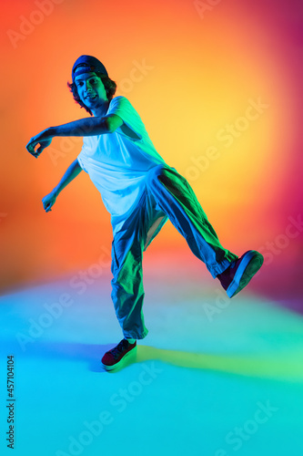 Close-up portrait of young man, hip-hop dancer in stylish clothes in action isolated on colorful background at dance hall in neon light.