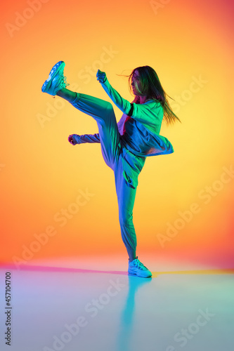 Portrait of young sportive girl dancing hip-hop in stylish clothes on colorful background at dance hall in neon light. Youth culture, movement, style and fashion, action.
