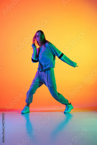 Young sportive girl dancing hip-hop in stylish clothes on colorful background at dance hall in neon light. Youth culture, movement, style and fashion, action.