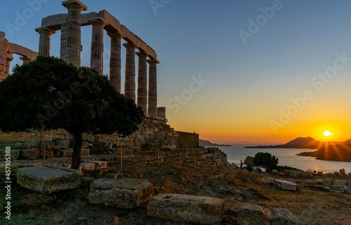 Cloudless sunset behind the mountains, with the sea. There is a Greek temple in the picture.