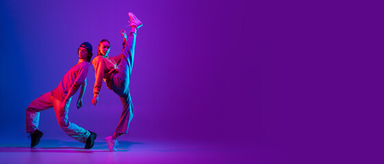 Flyer. Two dancers, young man and woman dancing hip-hop in casual sports youth clothes on gradient purple pink background at dance hall in neon light.