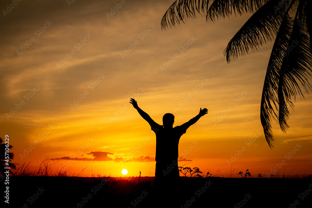 Silhouette of a man with arms outstretched towards the sky during sunset. Successful man.