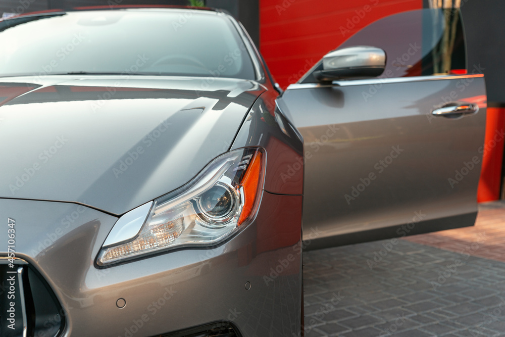 Front headlight of a metallic luxury modern car close up. Car with open door.