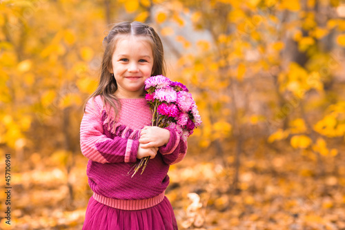 Cute little girl in fall park with pink flower bouquet.