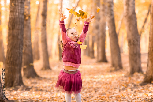 Cute little girl in autumn park throw up orange and yellow color leaves. Fall season.