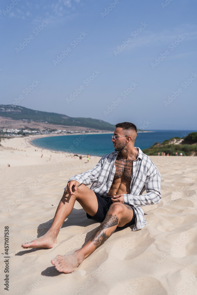 Chico atletico tatuado posando en dunas de arena