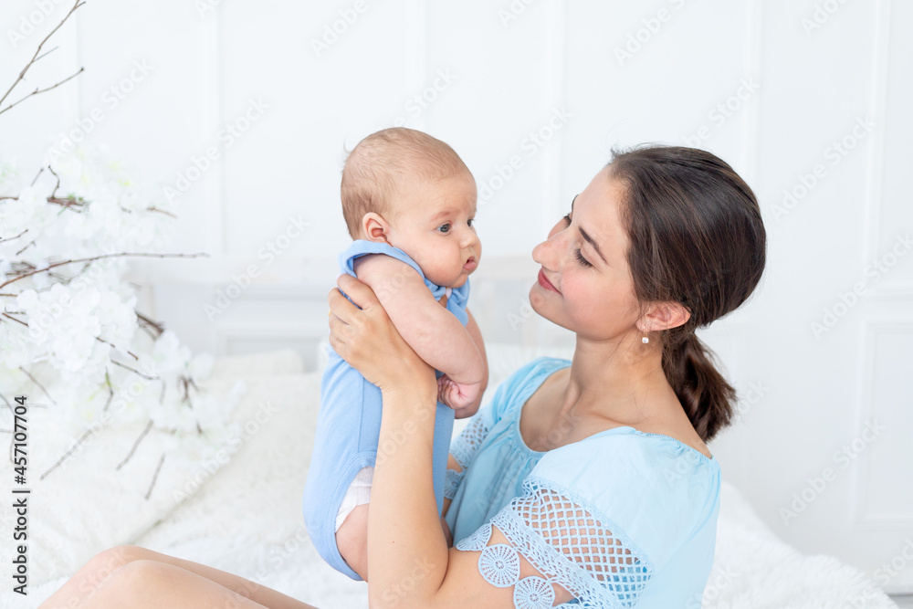 a young mother with a newborn baby gently embraces him at home on the bed, the concept of a happy family and birth
