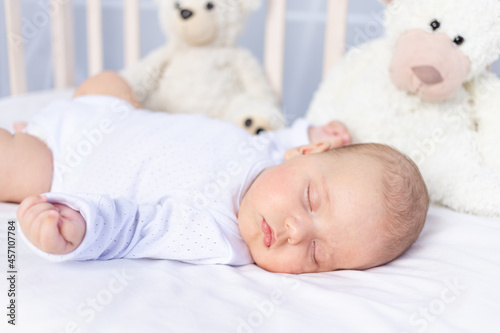 healthy sleep of a newborn baby in a crib in the bedroom with a soft toy bear on a cotton bed