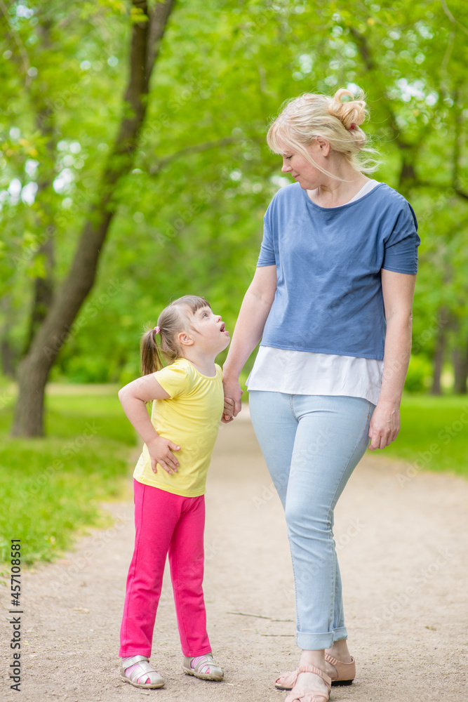 Fototapeta premium Little girl with syndrome down walks with her mother in a summer park