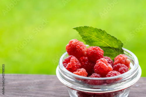 Fresh raspberries in bowl on wooden table on blurred nature background