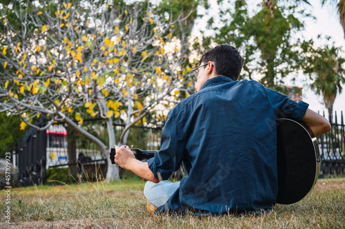 Photography Back view of a young caucasian boy tuning his guitar in the park.