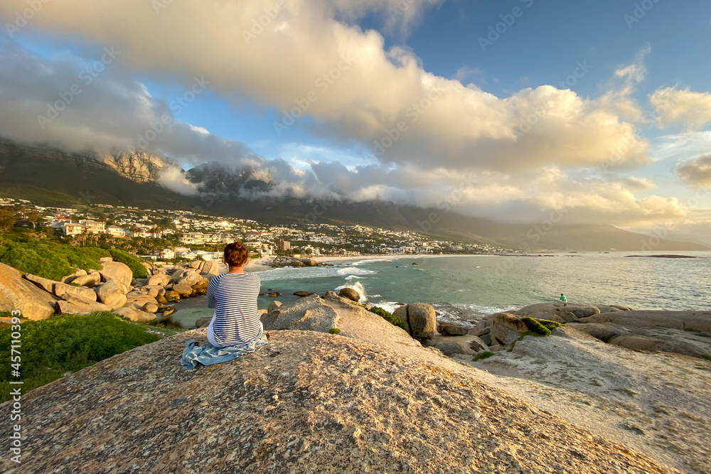 Woman sitting on a rock looking at Camps Bay, South Africa.