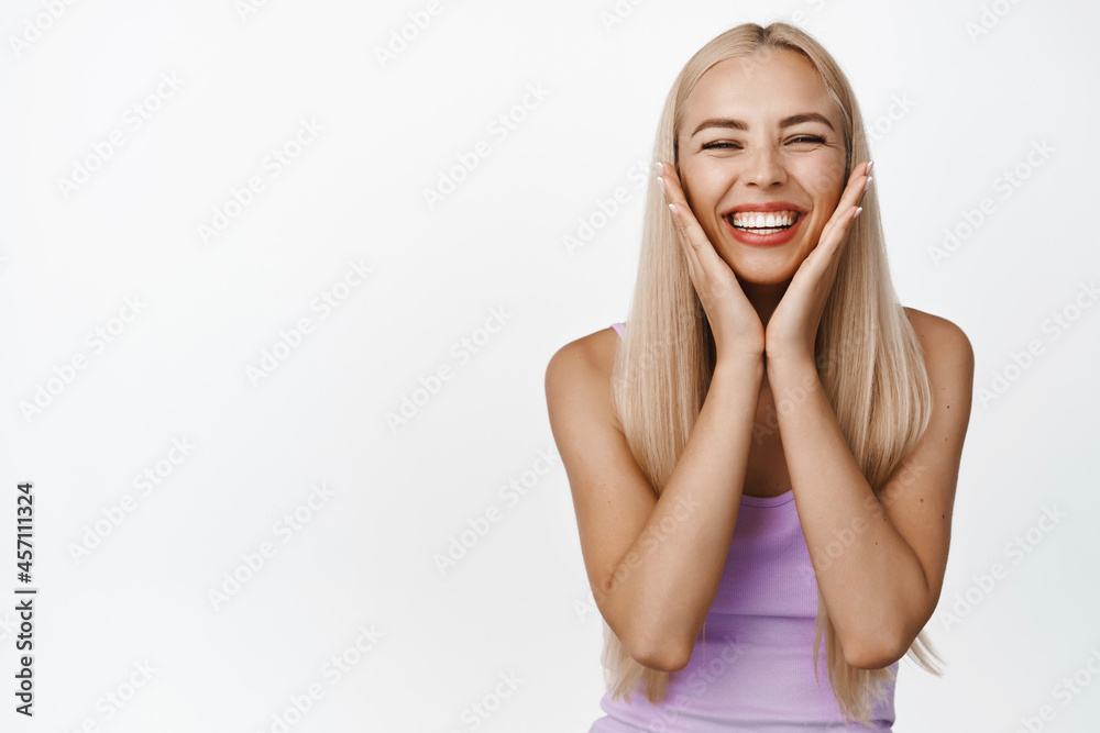 Beauty and wellbeing. Happy young natural girl touching her soft glowing skin, smiling satisfied with skincare product, standing over white background Beauty and wellbeing. Happy young natural girl touching her soft glowing skin, smiling satisfied with skincare product, standing over white background