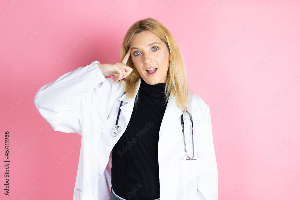 Young blonde doctor woman wearing stethoscope standing over isolated pink background smiling and thinking with her fingers on her head that she has an idea. Young blonde doctor woman wearing stethoscope standing over isolated pink background smiling and thinking with her fingers on her head that she has an idea.