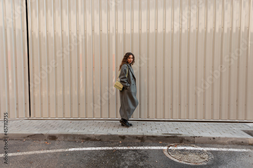 beautiful curly fashionable girl in fashion vintage clothes with a bag walks near a metal wall. Women s street style and beauty