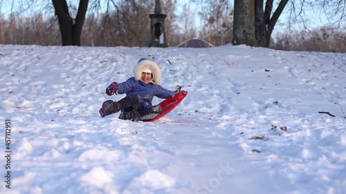 little girl goes downhill on an ice sled down the winter snow-covered hill photo