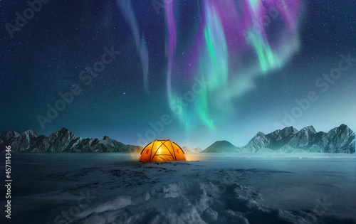 A tent pitched up in snow at night with the northern lights flickering in the sky above. Aurora Borealis and travelling. Photo composite. photo