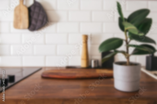 Kitchen brass utensils  chef accessories - blurred kitchen background . Hanging kitchen with white tiles wall and wood tabletop.Green plant on kitchen background