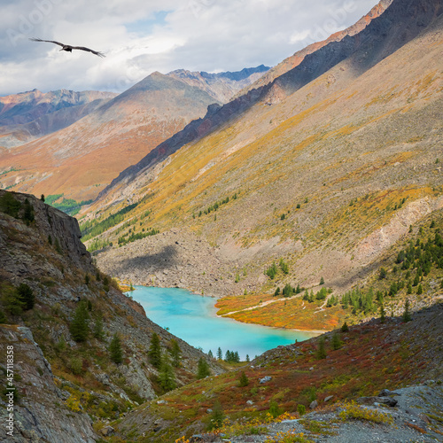 Upper Shavlin Lake in the Altai. Autumn alpine landscape with beautiful shallow mountain lake with streams in highland valley from bigger mountains under cloudy sky.