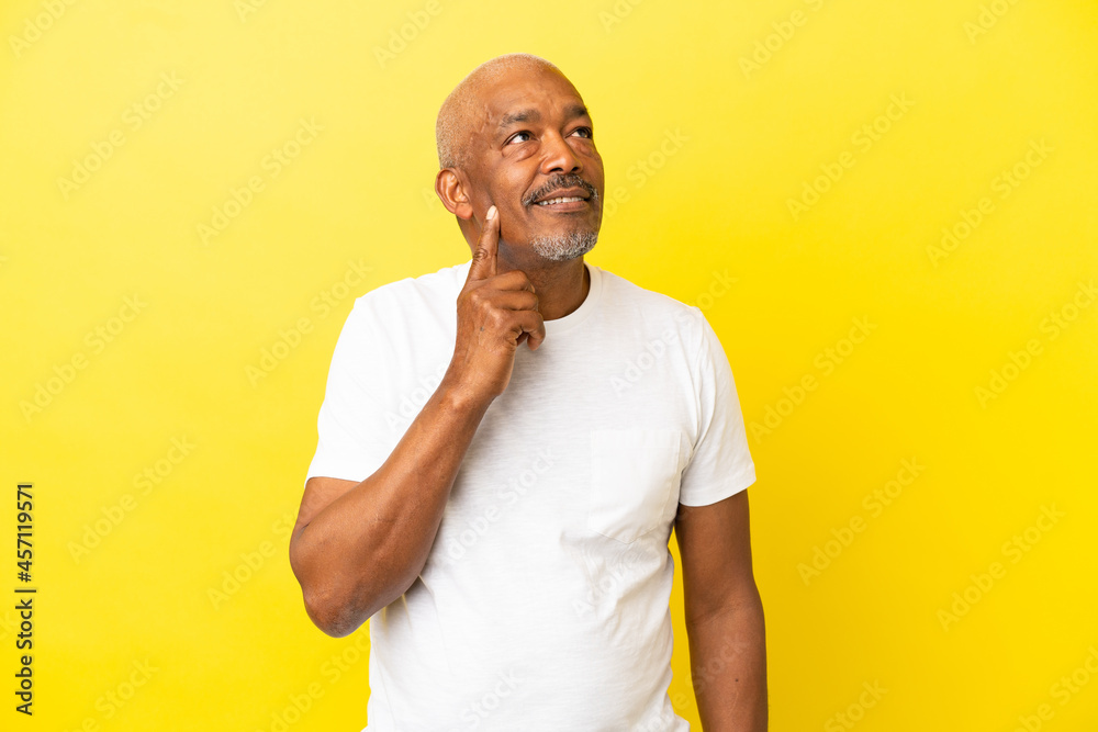 Cuban Senior isolated on yellow background thinking an idea while looking up Cuban Senior isolated on yellow background thinking an idea while looking up