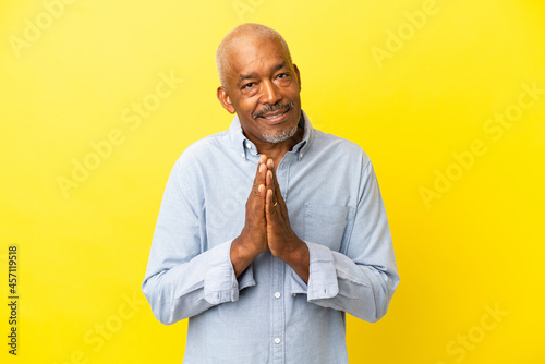 Cuban Senior isolated on yellow background keeps palm together. Person asks for something