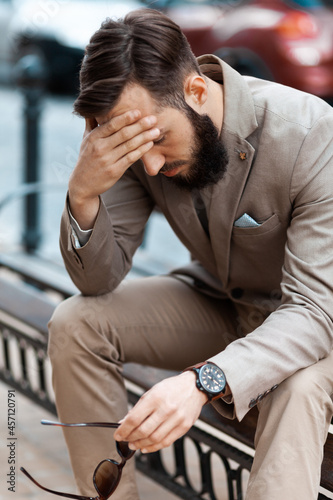 The bearded man on the street got sick. An entrepreneur has a headache because of.work. The businessman sat down on a bench to rest.