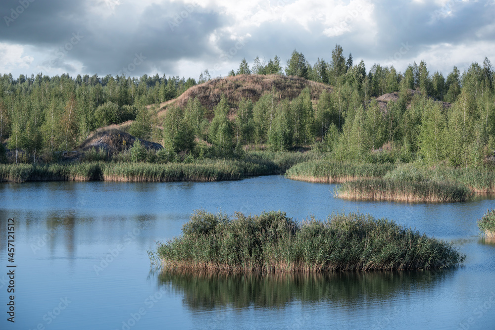 A lake with a plane surface and reflections against the blue sky and white clouds. Originated from an old quarry flooded, groups of islands overgrown with reeds. A lake with a plane surface and reflections against the blue sky and white clouds. Originated from an old quarry flooded, groups of islands overgrown with reeds.