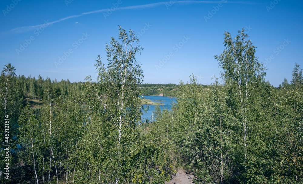 A blue tranquil lake with scattered islets of reed and surrounded by birches on its shores. A quarry flooded as a result of human activity. Summertime. A blue tranquil lake with scattered islets of reed and surrounded by birches on its shores. A quarry flooded as a result of human activity. Summertime.