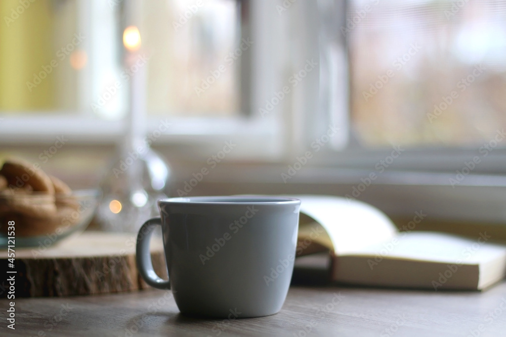 Fototapeta premium Bowl of cookies, cup of hot beverage, open book and lit candles on a table. Selective focus.