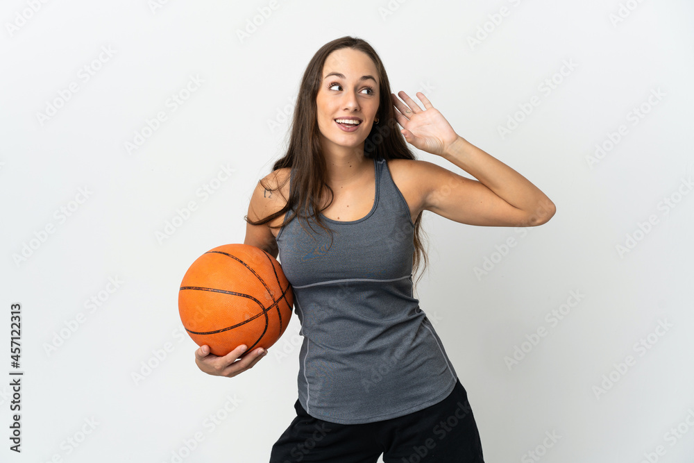 Young woman playing basketball over isolated white background listening to something by putting hand on the ear Young woman playing basketball over isolated white background listening to something by putting hand on the ear