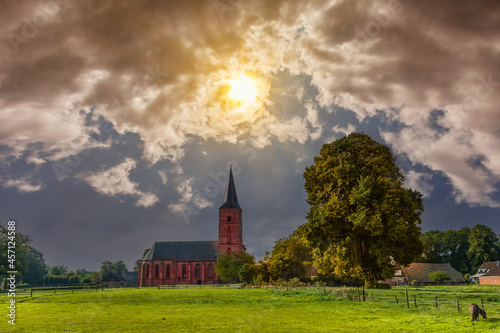 Drenthe landscape with Gothic Jacobus church and bell tower built in the 15th century in Rolde in the Dutch province of Drenthe against  breaking sunlight photo