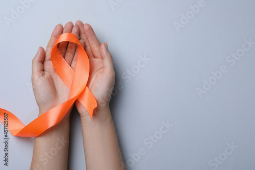 Woman holding orange ribbon on light grey background, top view with space for text. Multiple sclerosis awareness photo