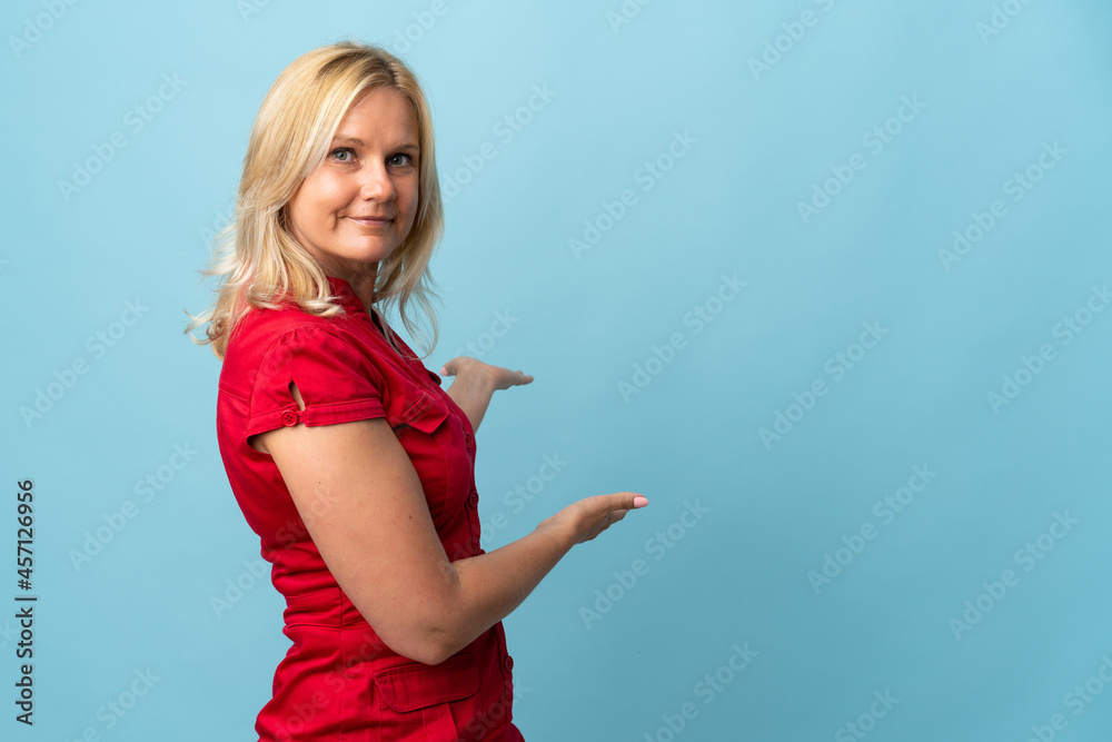 Middle age woman isolated on blue background extending hands to the side for inviting to come Middle age woman isolated on blue background extending hands to the side for inviting to come