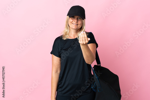 Middle age woman with sport bag isolated on pink background inviting to come with hand. Happy that you came