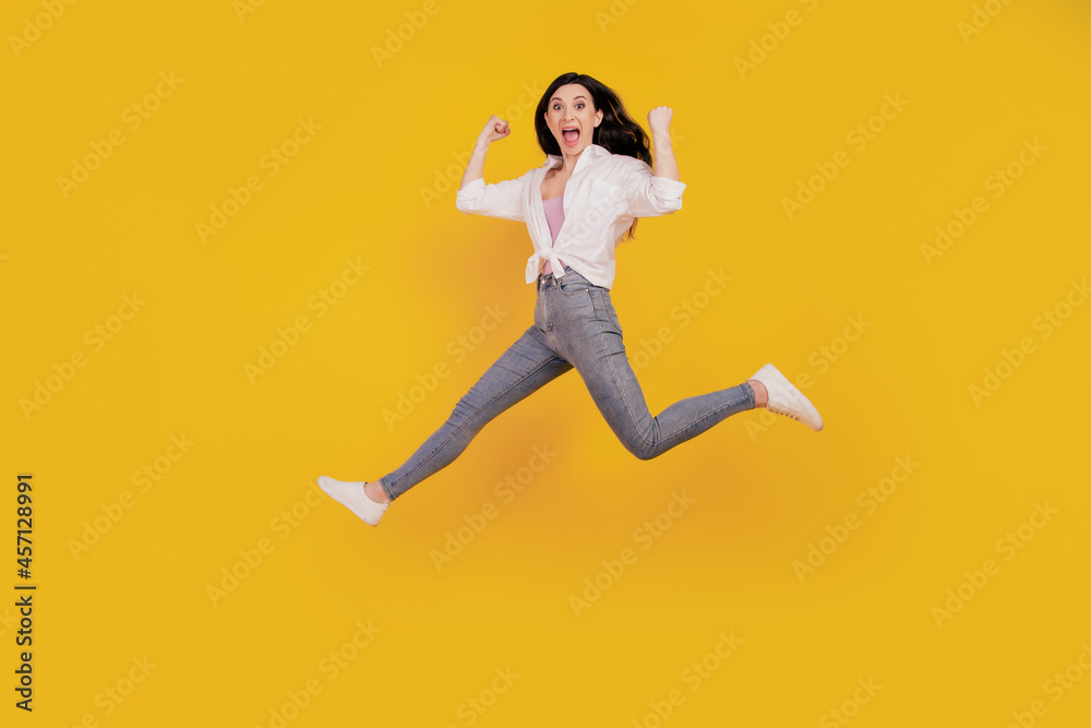 Portrait of crazy sporty active girl raise fists open mouth jump run on yellow background