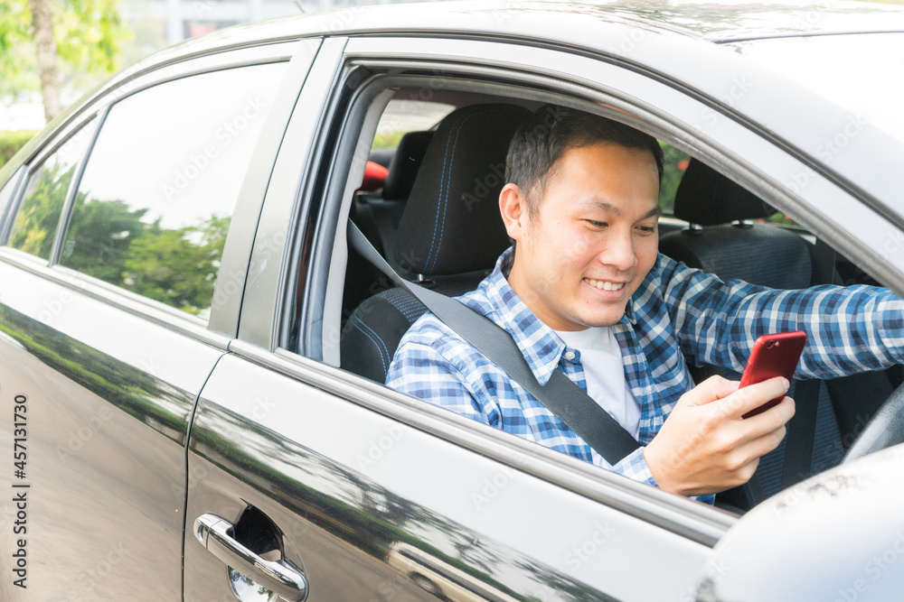 Handsome young asian man smiling using a smartphone in his car and looking at smartphone. Travel concept. socail concept Handsome young asian man smiling using a smartphone in his car and looking at smartphone. Travel concept. socail concept