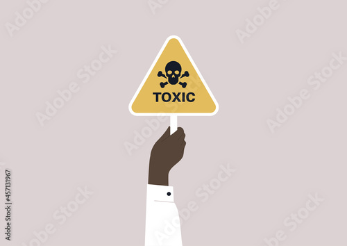 A hand holding a yellow triangle toxic sign with a skull and crossbones