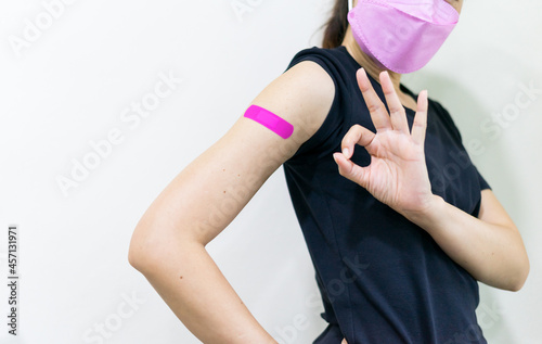 Asian woman wear face mask using adhesive bandage with at arm and showing O.K. gesture after injection vaccine. Covid 19 vaccine disease preparing.