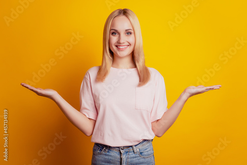 Portrait of cheerful dreamy girl palms hold blank spaces on yellow background