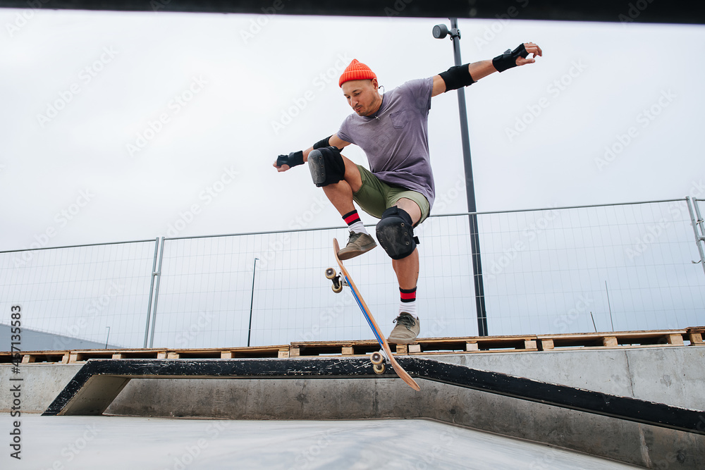Agile mature skater in a watch cap doing tricks with a skateboard at skate park