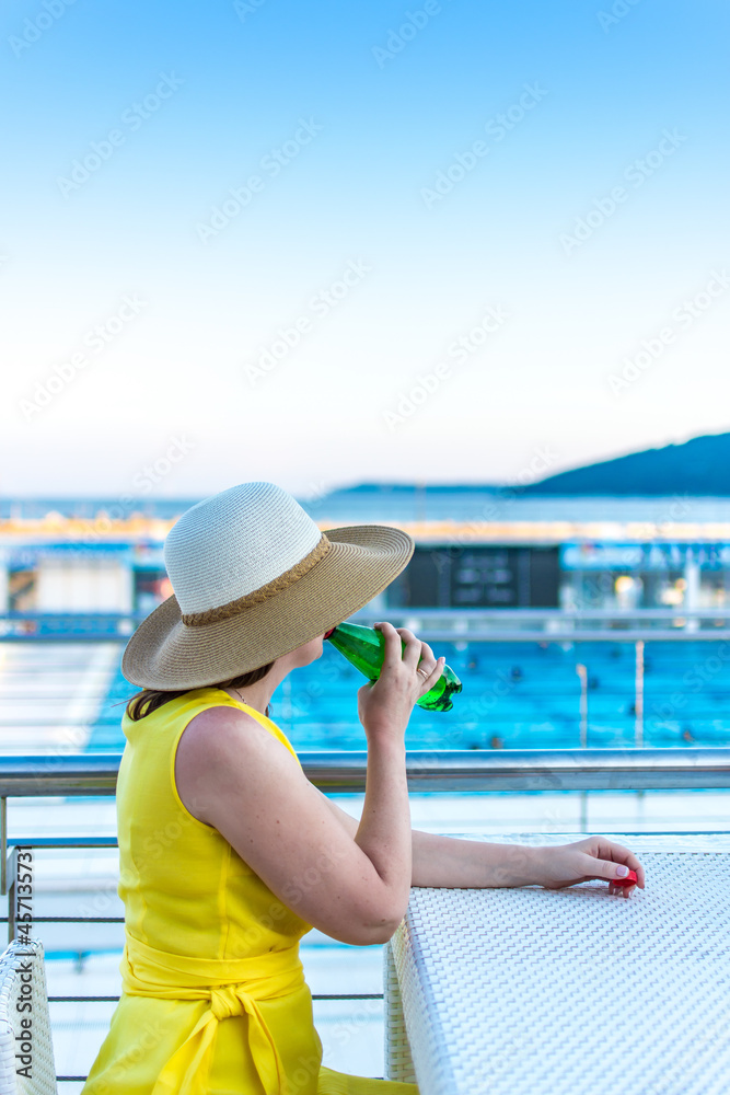 Elegant woman in a yellow dress drinking from a bottle on the sea beach