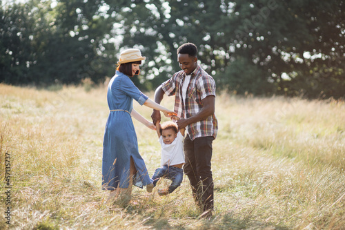 Beautiful multi ethnic parents in casual wear playing with little happy son on field. Positive family relaxing together on fresh air. Summer time and lifestyles concept.