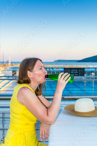 Elegant woman in a yellow dress drinking from a bottle on the sea beach