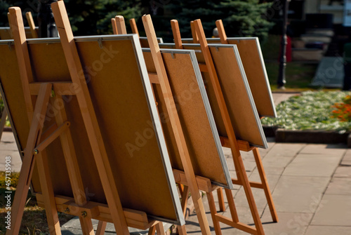 Lots of easels on the street. Easels with blank canvases close up. Layout for design.