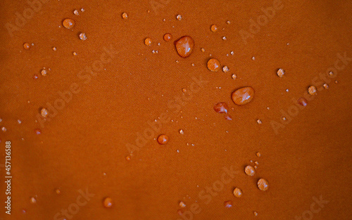 Water drops on a waterproof fabric for mountain clothes. Detail photo of orange wateproof jacket with water droplets on it. Jacket using the gore tex technology. photo